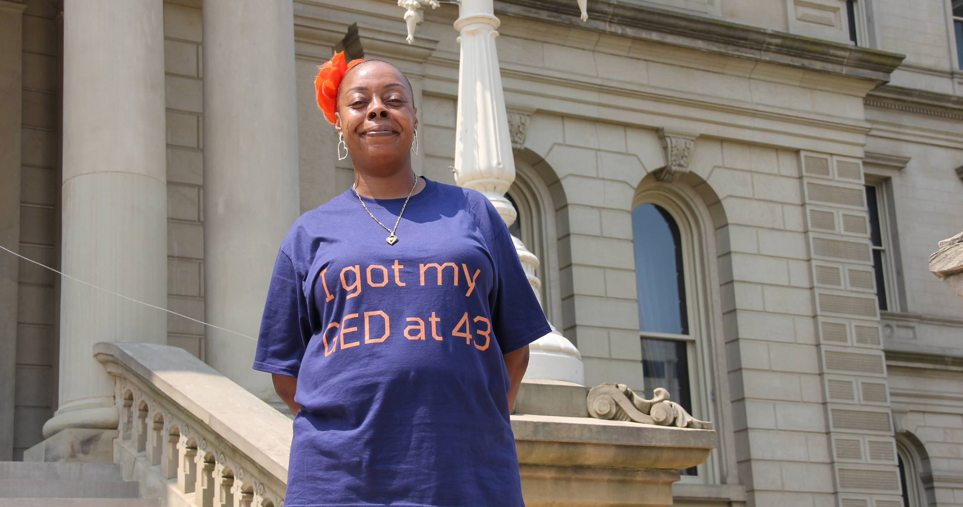 A smiling woman wearing a shirt with the text "i got my ged at 43" printed on it